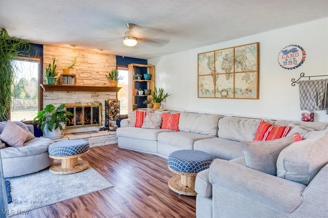 Living room featuring wood finished floors, ceiling fan, a textured ceiling, and a fireplace