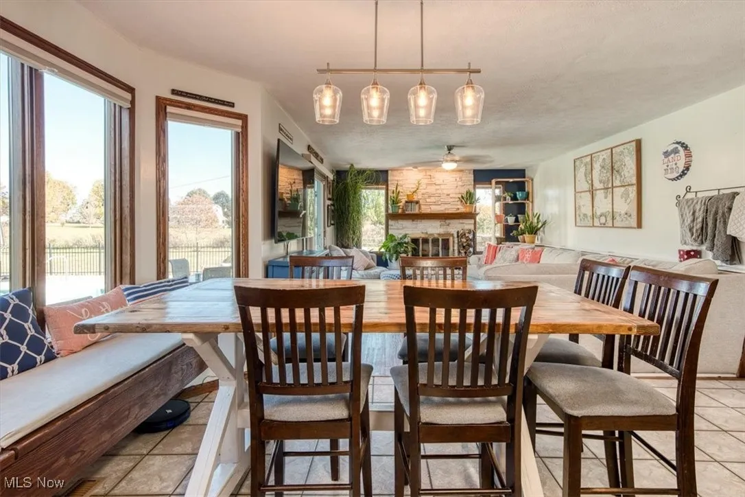 Dining room with a fireplace, ceiling fan, light tile patterned flooring, and a textured ceiling