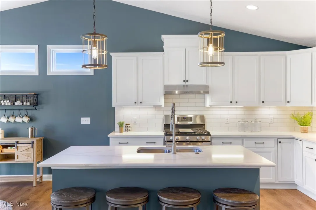 Kitchen featuring pendant lighting, vaulted ceiling, white cabinets, and stainless steel range with gas stovetop