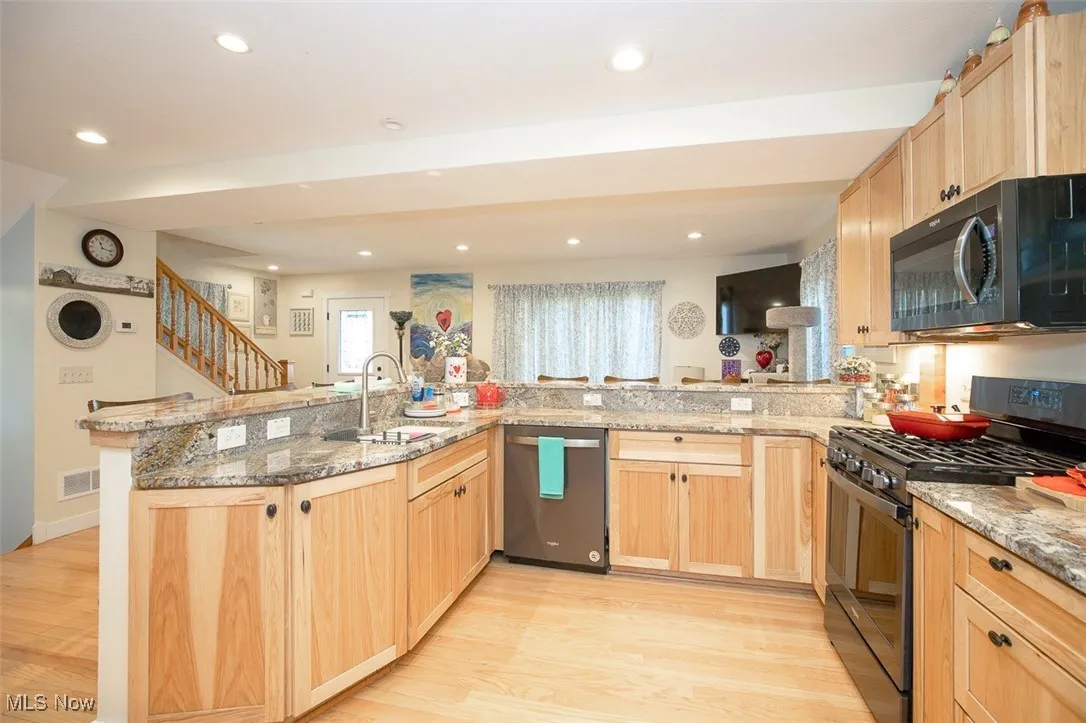 Kitchen featuring granite countertops, a kitchen bar, maple wood floors, stainless steel range, and recessed lighting
