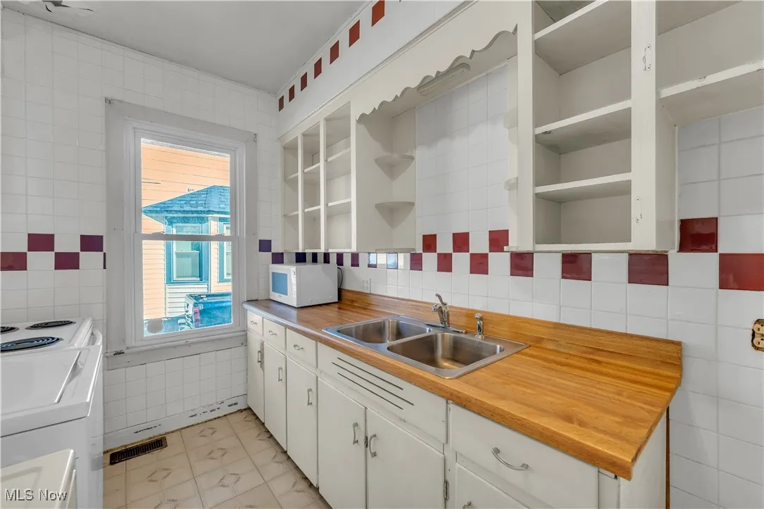 Kitchen with open shelves, tile walls, white cabinetry, and white appliances