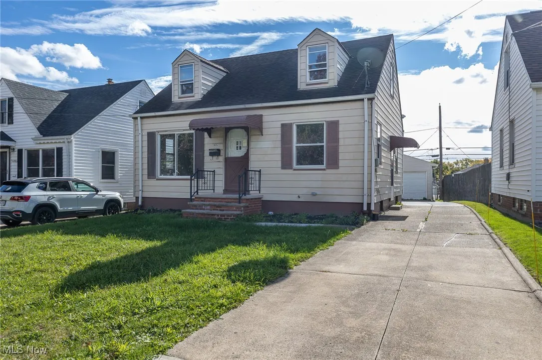 Cape cod-style house featuring a front yard, roof with shingles, and a detached garage