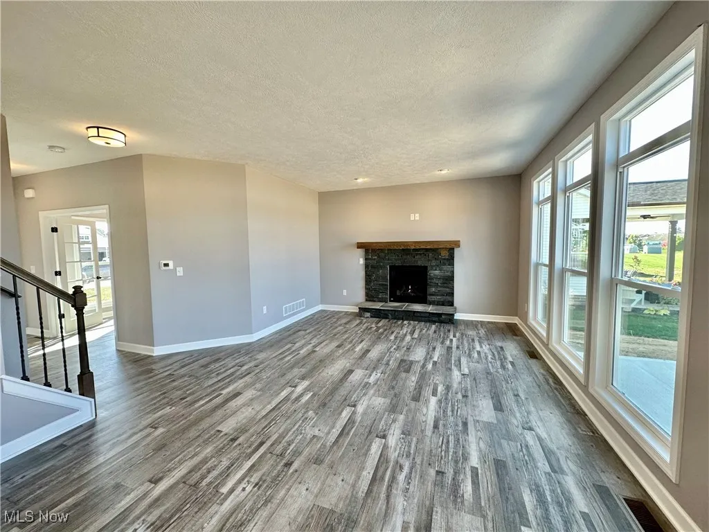 Unfurnished living room with dark hardwood / wood-style flooring, a textured ceiling, and a stone fireplace