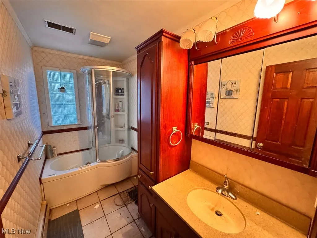 Bathroom featuring wallpapered walls, combined bath / shower with glass door, crown molding, vanity, and light tile patterned flooring