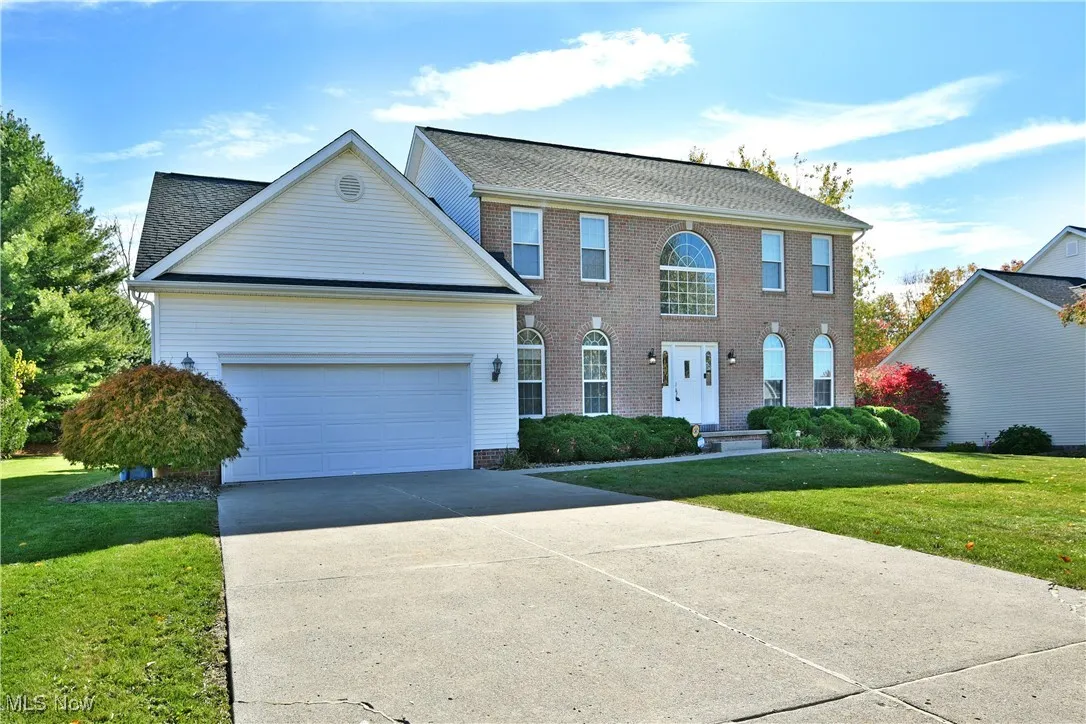 Colonial house featuring a front lawn, driveway, a garage, and a shingled roof