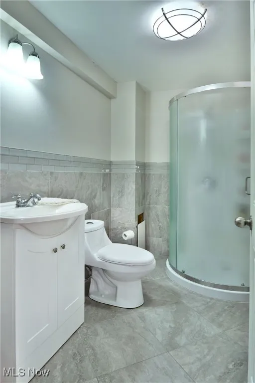 Full bath with tile walls, vanity, a shower stall, wainscoting, and tile patterned floors