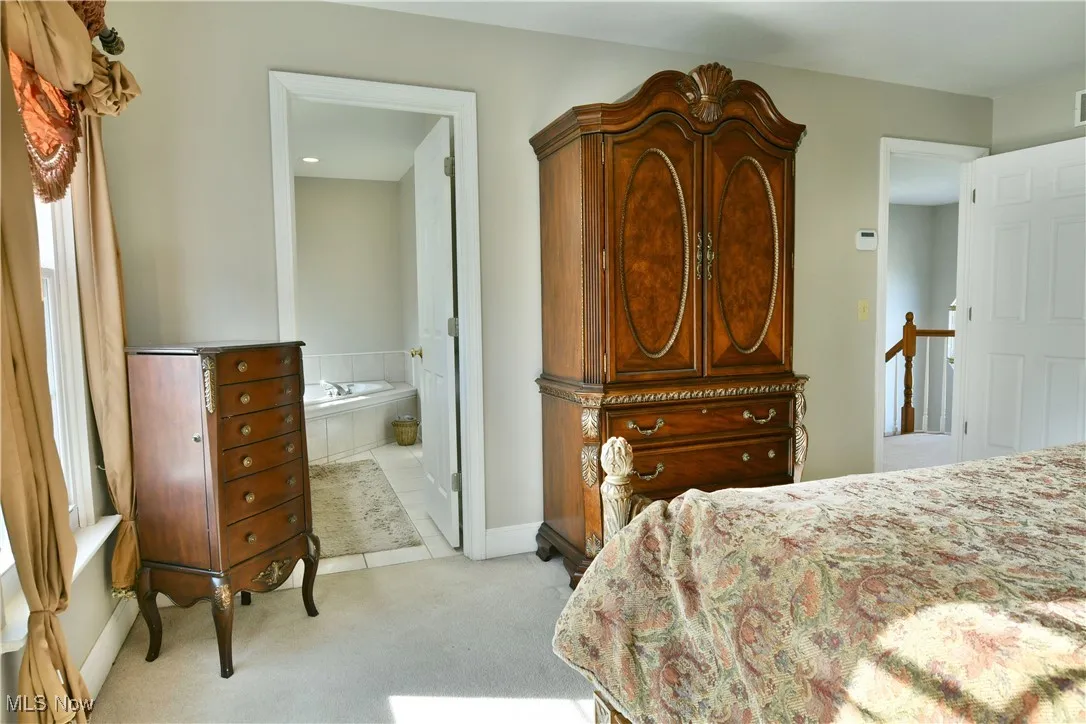 Bedroom with light carpet, ensuite bathroom, and light tile patterned floors
