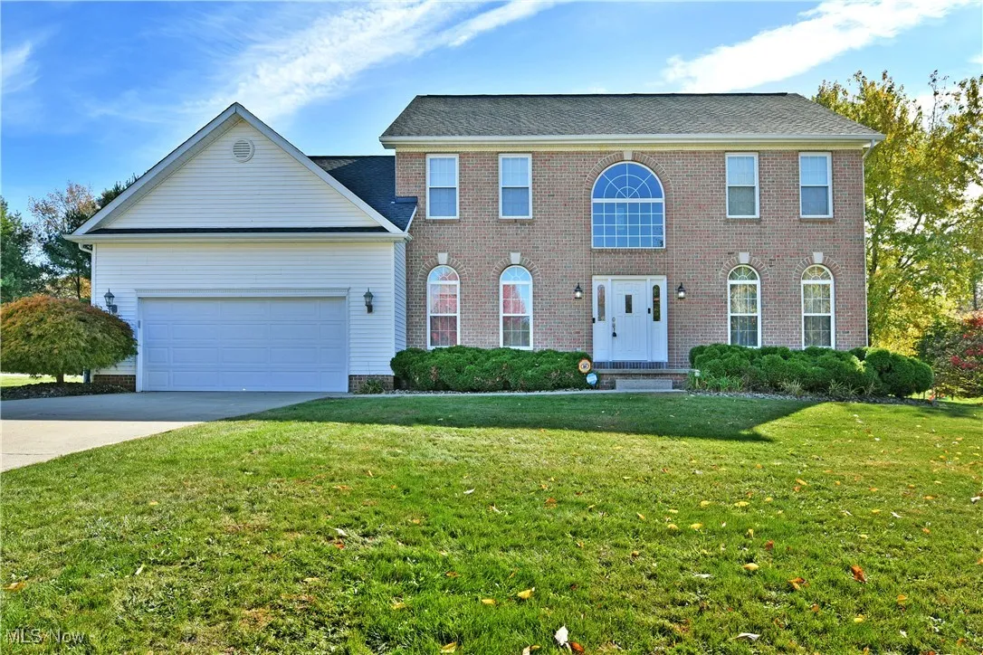 Colonial home with concrete driveway, a front lawn, an attached garage, and brick siding
