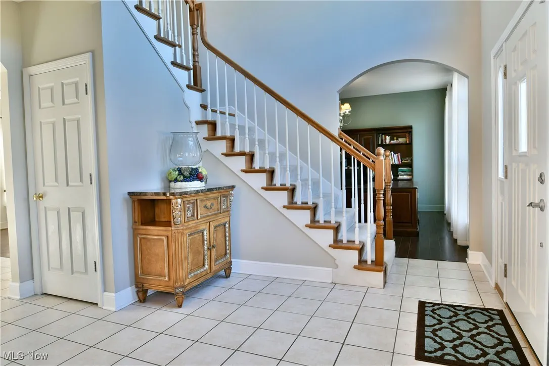 Foyer featuring arched walkways, light tile patterned floors, and stairs