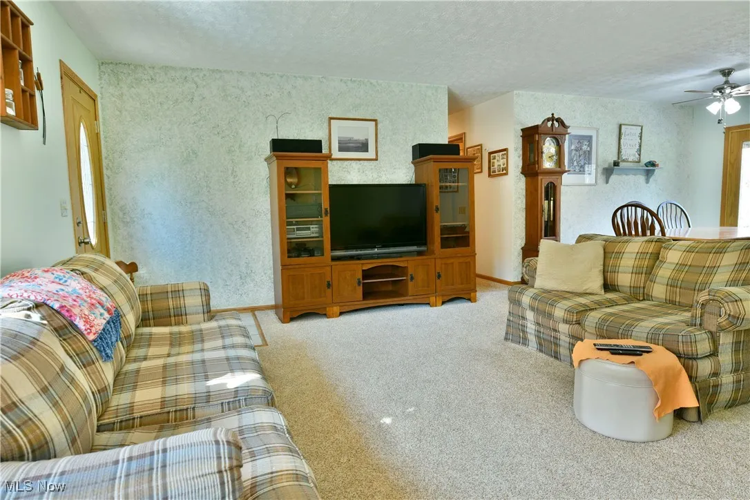 Living room featuring a ceiling fan, light colored carpet, a textured ceiling, and wallpapered walls