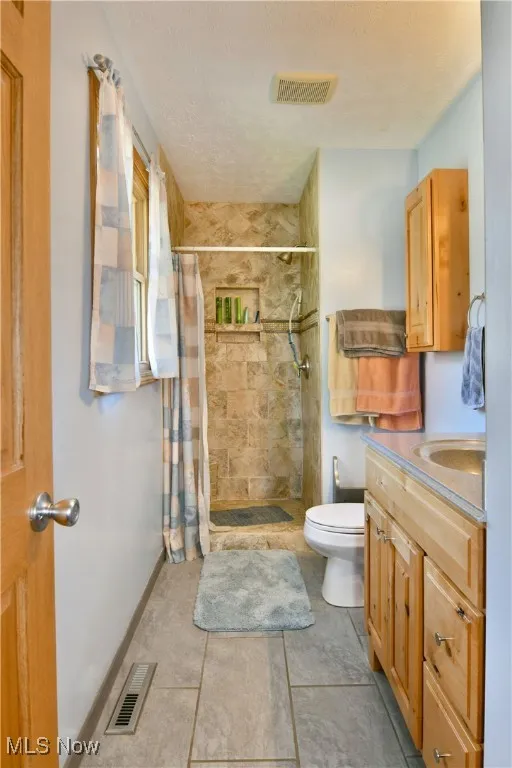 Bathroom featuring a textured ceiling, a shower stall, vanity, and light tile patterned flooring