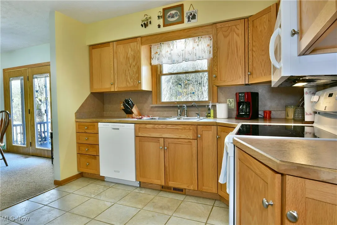 Kitchen featuring white appliances, tasteful backsplash, light countertops, light tile patterned floors, and brown cabinets