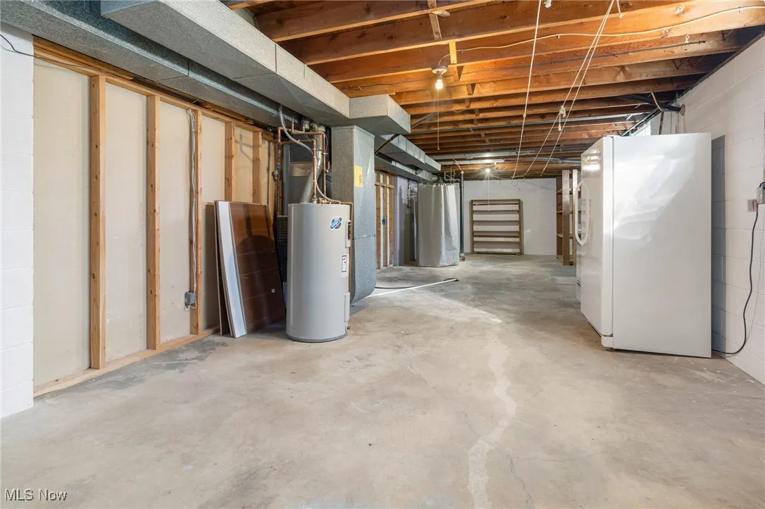Unfinished below grade area with freestanding refrigerator, water heater, and heating unit