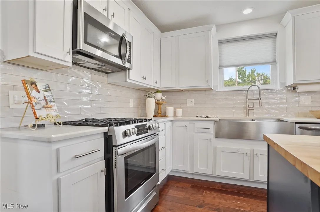 Kitchen with appliances with stainless steel finishes, white cabinetry, tasteful backsplash, butcher block counters, and dark wood finished floors