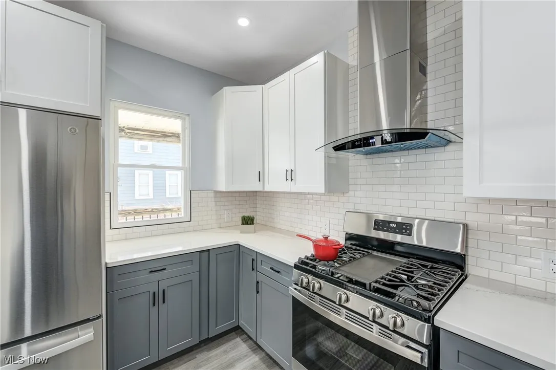 Kitchen with wall chimney range hood, gray cabinets, backsplash, and stainless steel appliances