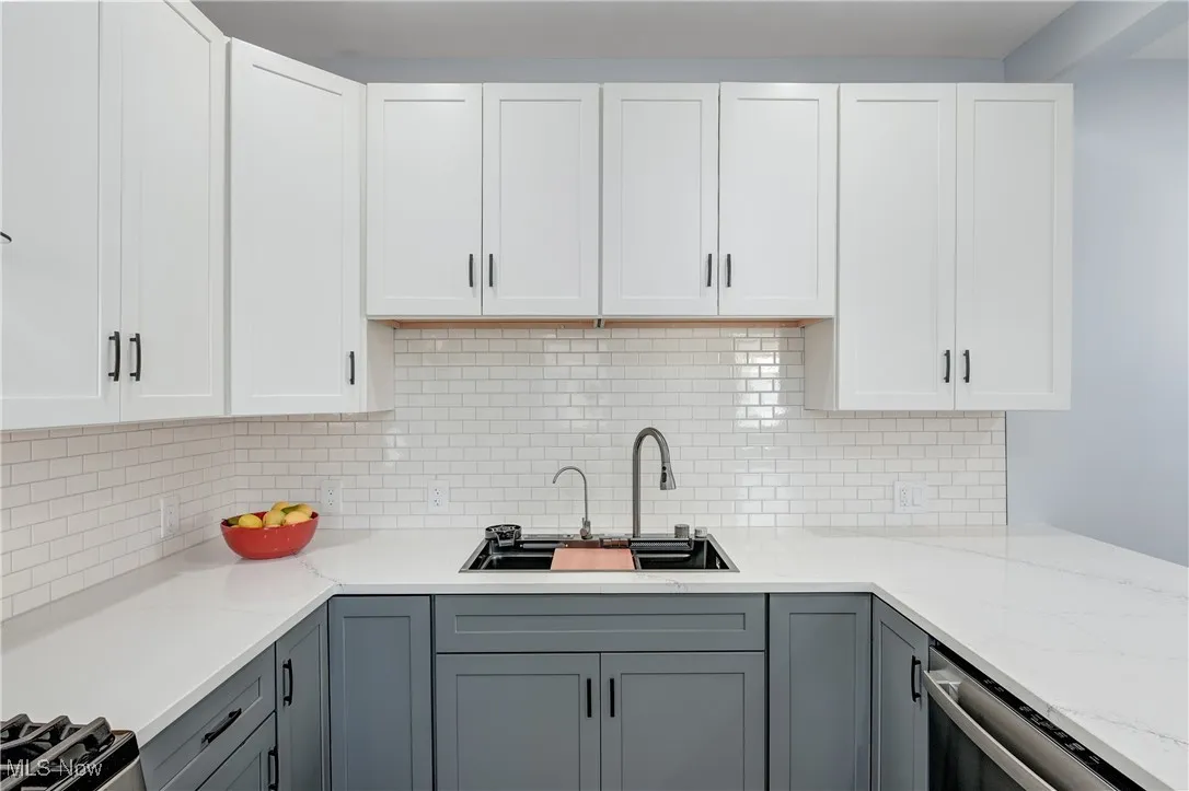 Kitchen featuring gray cabinets, a sink, light stone counters, white cabinets, and decorative backsplash