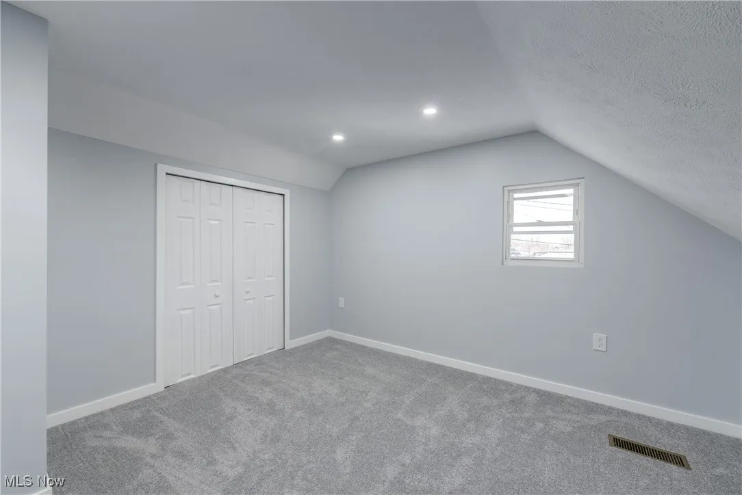 Additional living space with lofted ceiling, carpet, visible vents, and baseboards