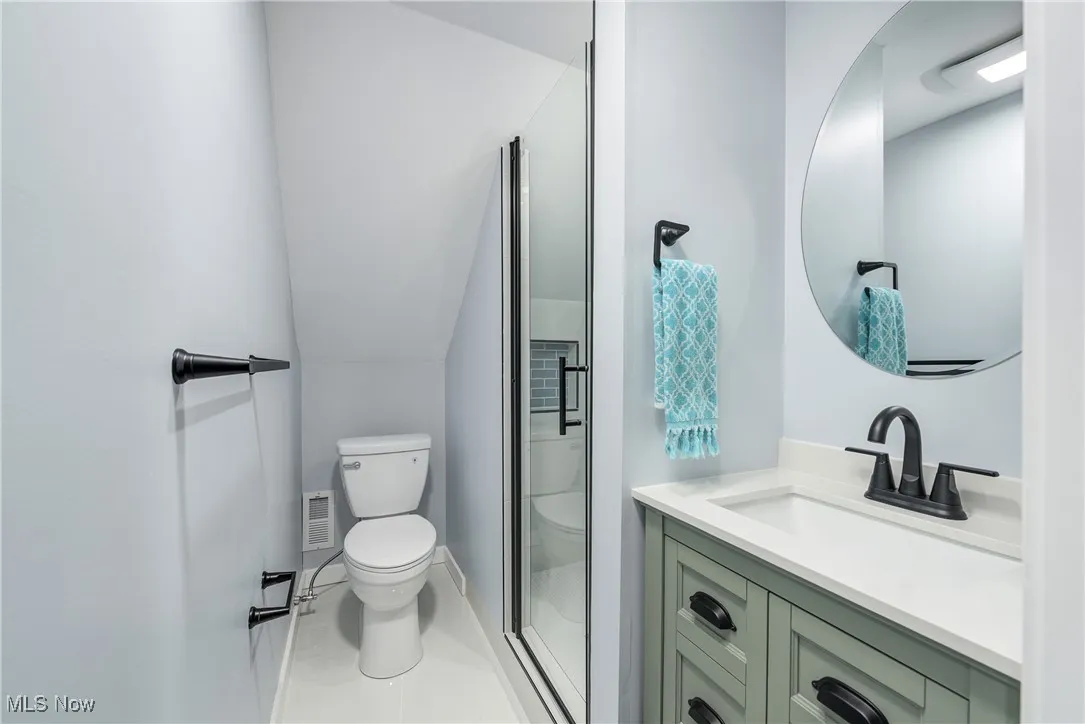 Bathroom featuring visible vents, toilet, a stall shower, vanity, and vaulted ceiling