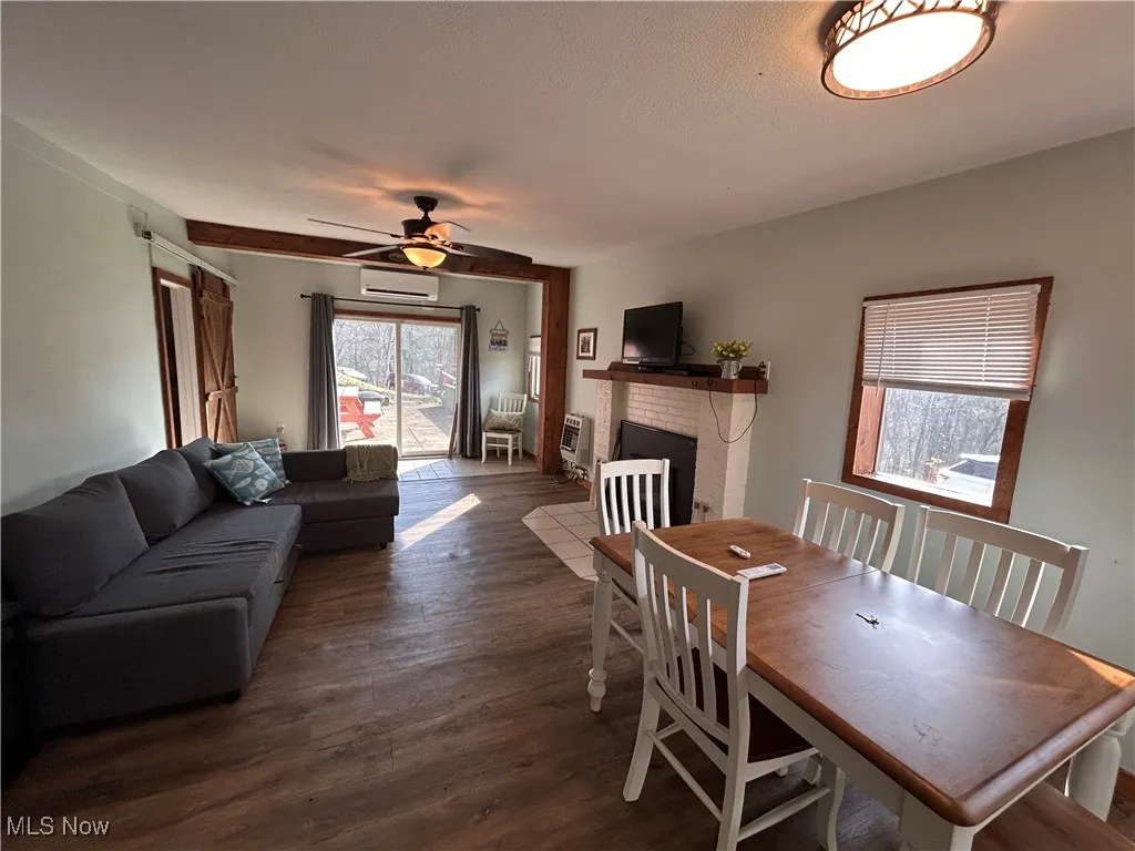Dining area featuring a wall mounted air conditioner, heating unit, wood finished floors, ceiling fan, and a fireplace