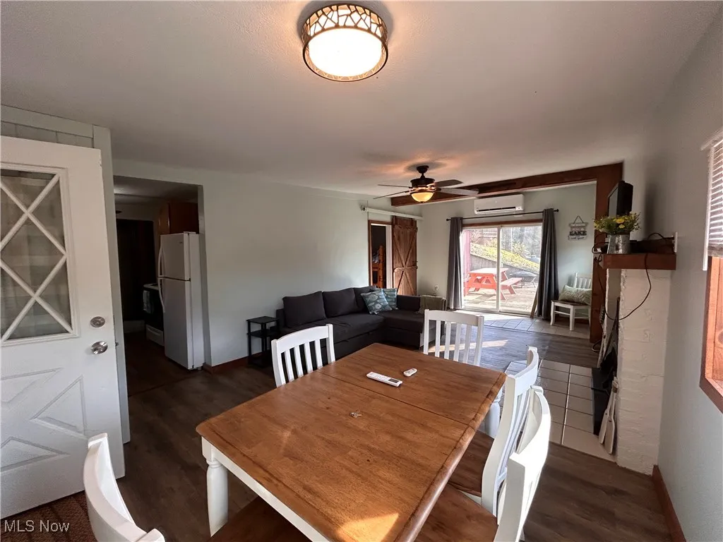 Dining room featuring an AC wall unit, baseboards, dark wood-style flooring, and a ceiling fan