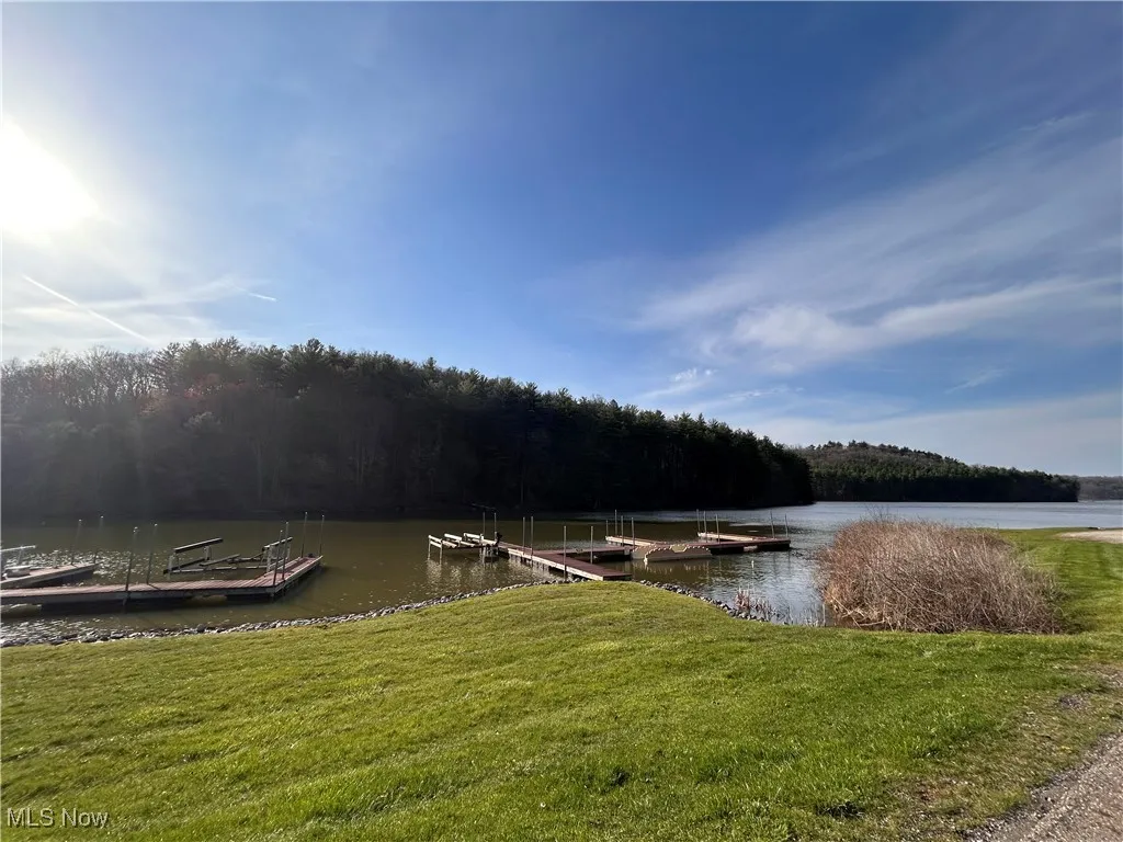 View of dock featuring a lawn, a water view, and a wooded view