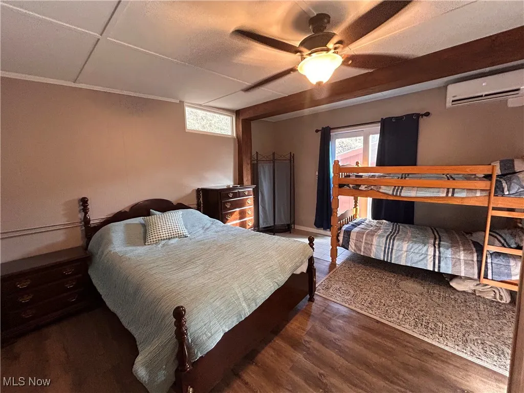 Bedroom featuring wood finished floors, an AC wall unit, and ceiling fan