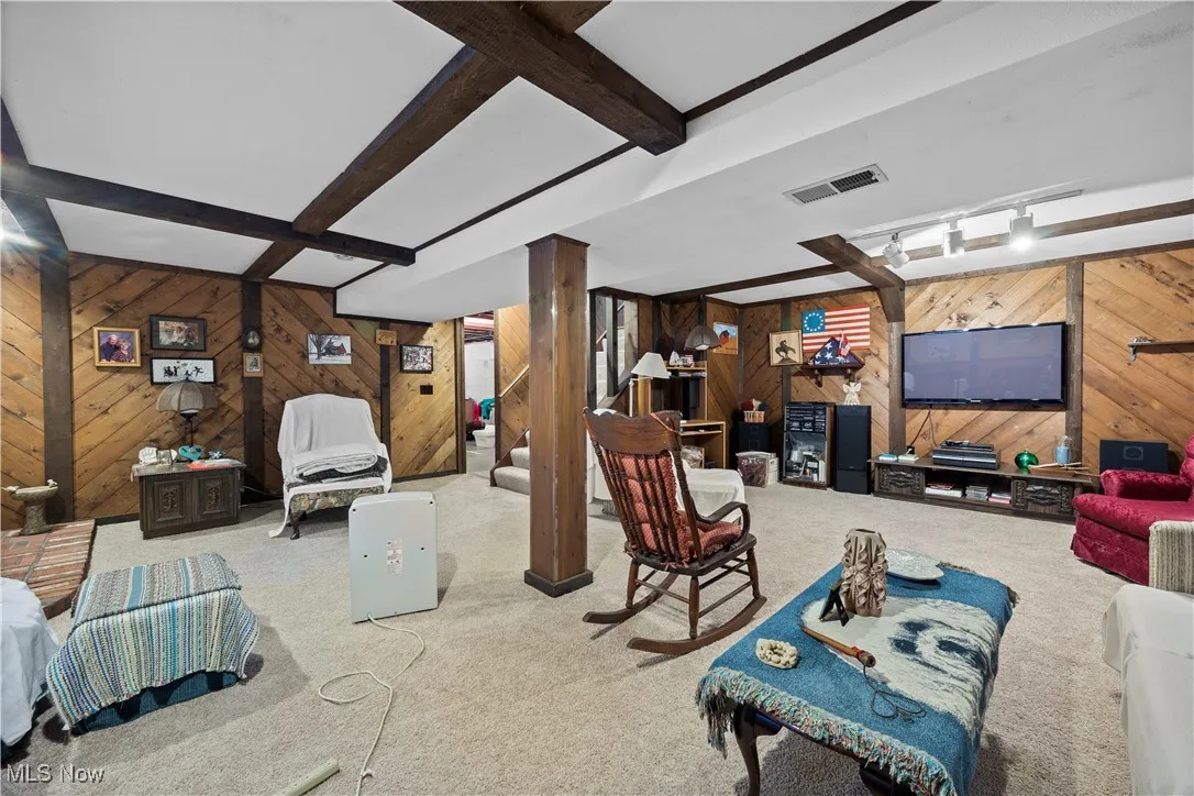 Carpeted living area with wooden walls and beam ceiling