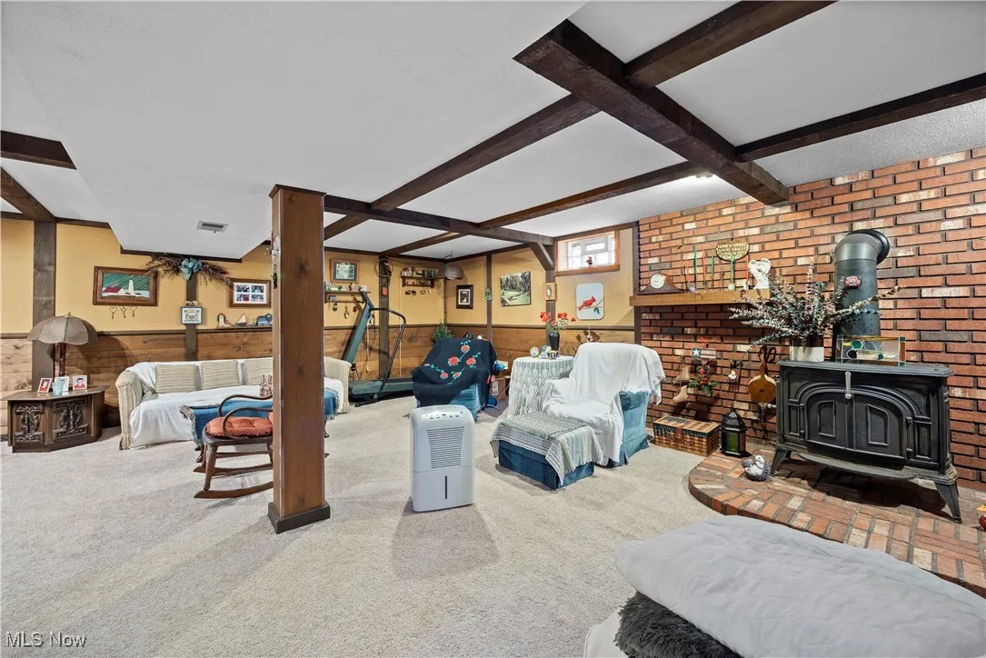 Carpeted living room featuring a wood stove, beam ceiling, coffered ceiling, and wood walls