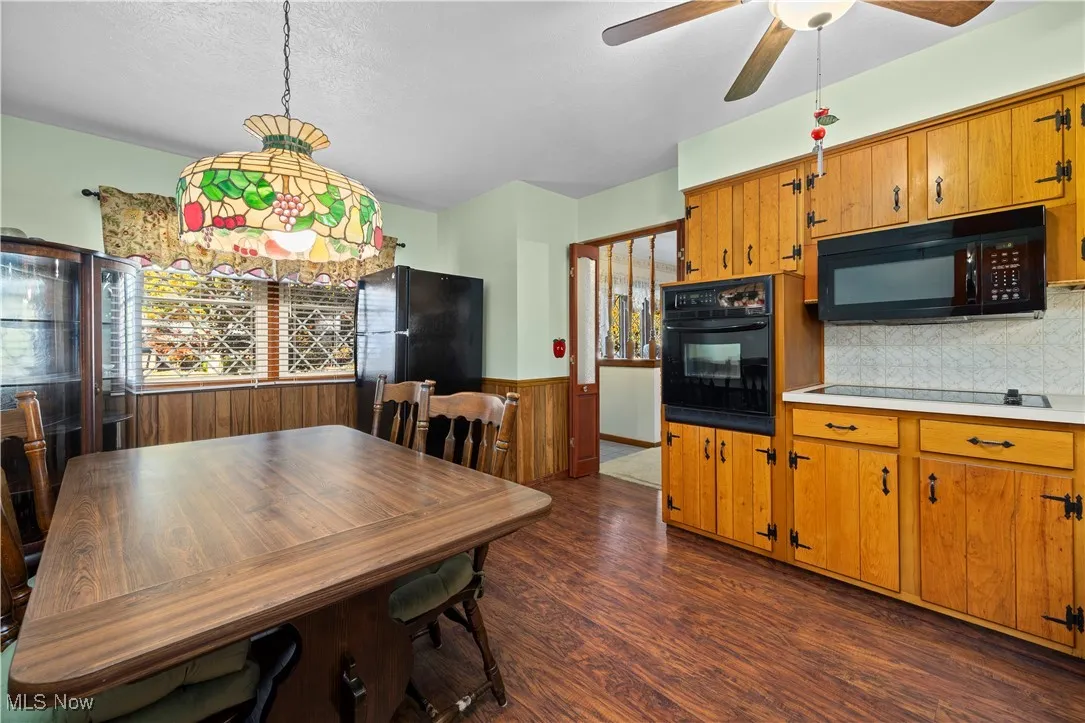 Kitchen with light countertops, dark wood finished floors, black appliances, brown cabinetry, and pendant lighting
