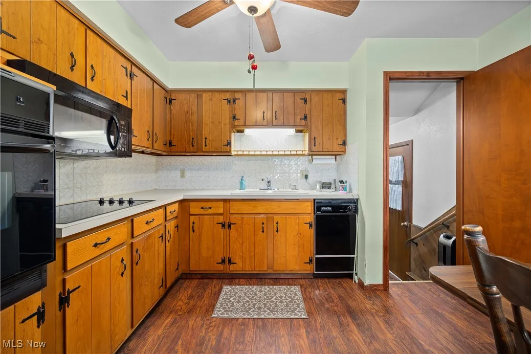 Kitchen featuring light countertops, dark wood-style flooring, black appliances, and backsplash