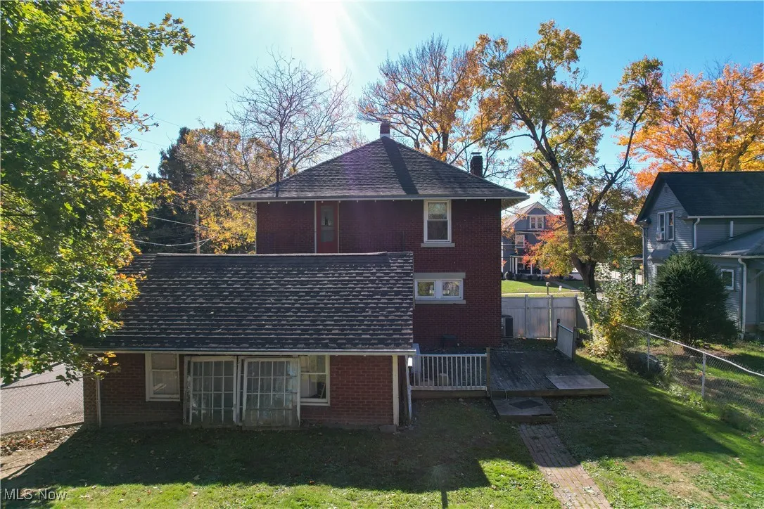 Rear view of property featuring a wooden deck, a fenced backyard, brick siding, roof with shingles, and a chimney
