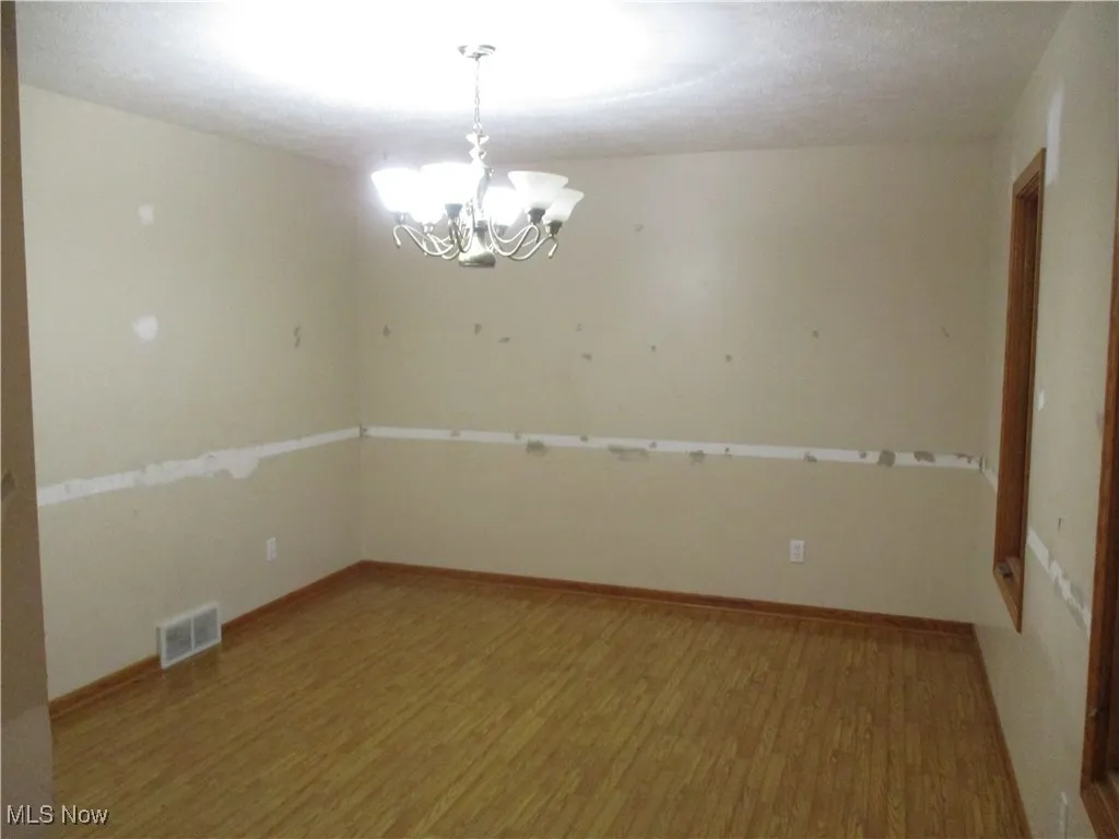 Spare room with wood finished floors and a chandelier