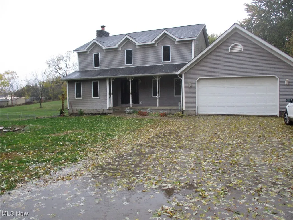 View of front of property featuring covered porch, a front lawn, a chimney, driveway, and an attached garage