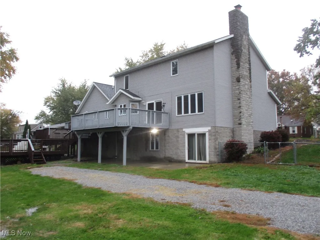 Back of house with a wooden deck, a chimney, and a patio