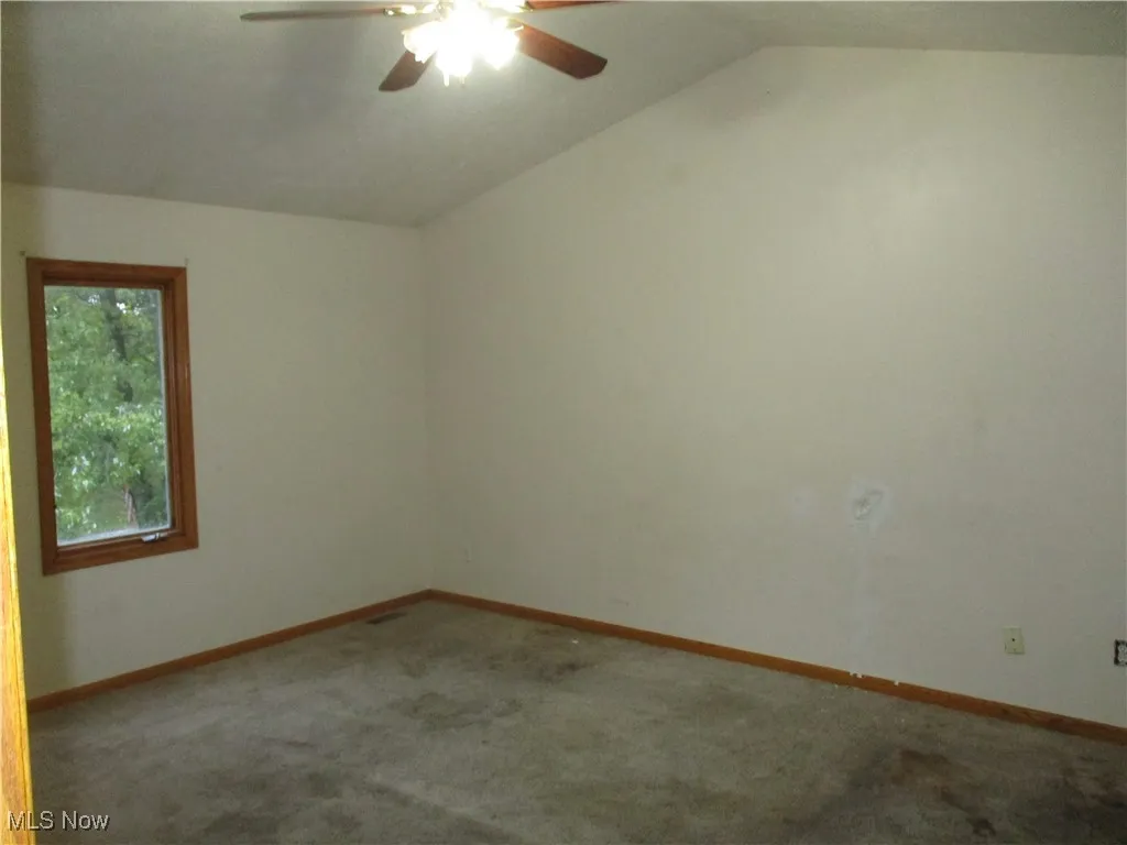 Unfurnished room featuring carpet floors, ceiling fan, and vaulted ceiling
