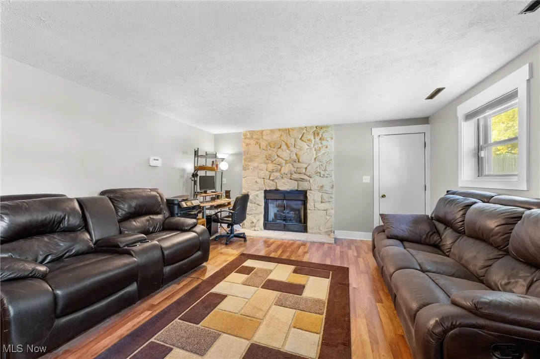 Living room with wood finished floors, a textured ceiling, a desk, and a fireplace