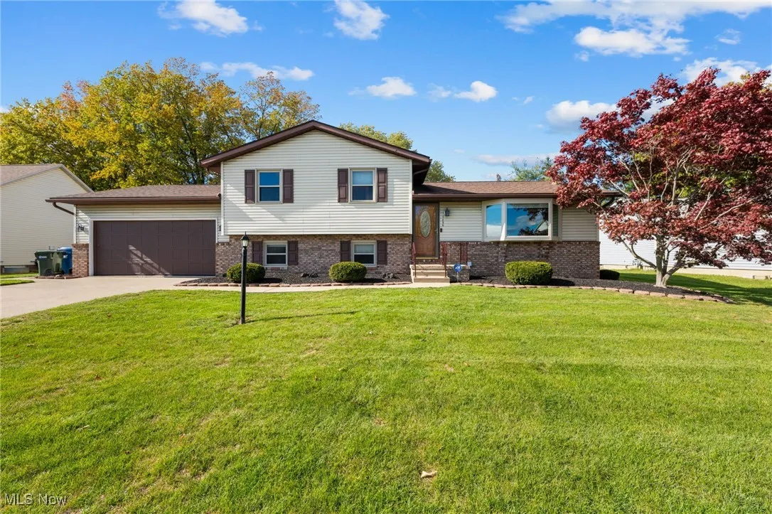 Tri-level home with brick siding, concrete driveway, an attached garage, and a front yard