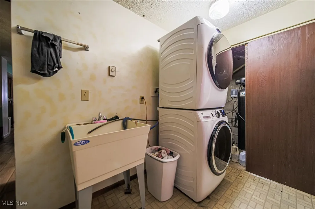 Washroom with stacked washer and clothes dryer, a textured ceiling, and brick patterned floors