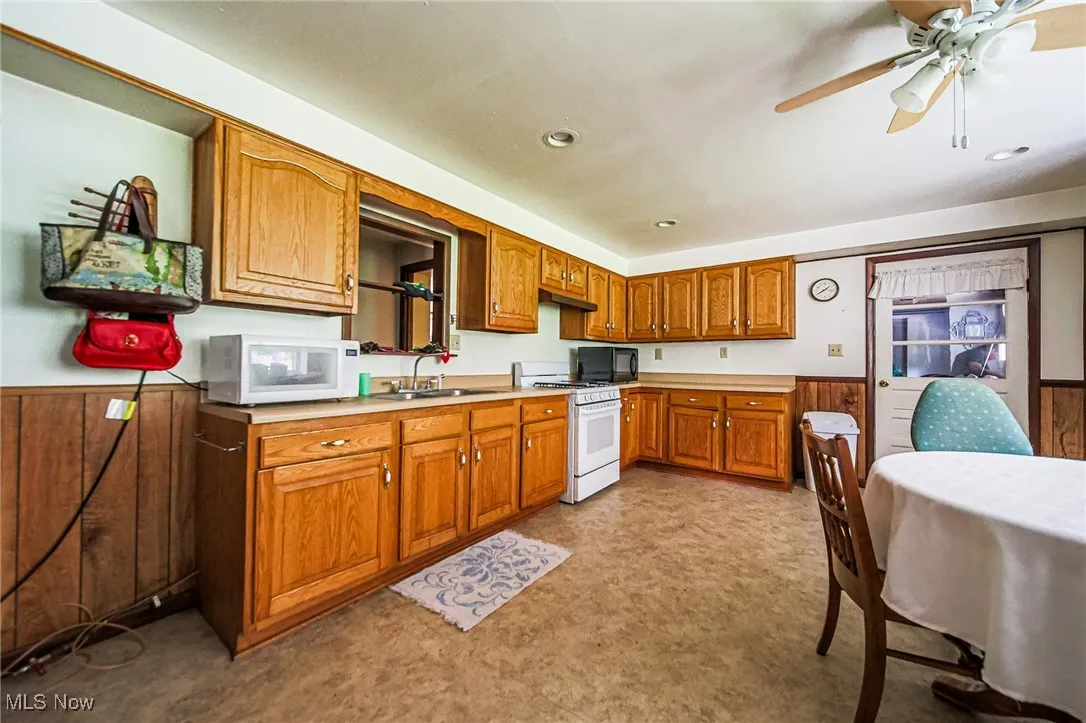 Kitchen with a wainscoted wall, wood walls, light countertops, brown cabinets, and white appliances