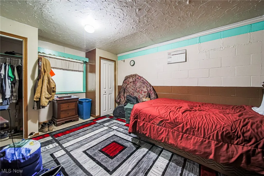Bedroom with concrete block wall, a closet, and a textured ceiling
