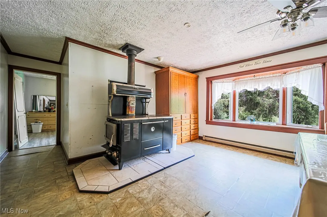 Kitchen featuring crown molding, a baseboard heating unit, a wood stove, a ceiling fan, and a textured ceiling