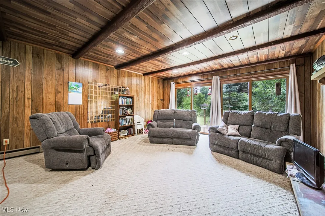 Carpeted living room featuring wooden walls, recessed lighting, a wood ceiling with exposed beams, and baseboard heating