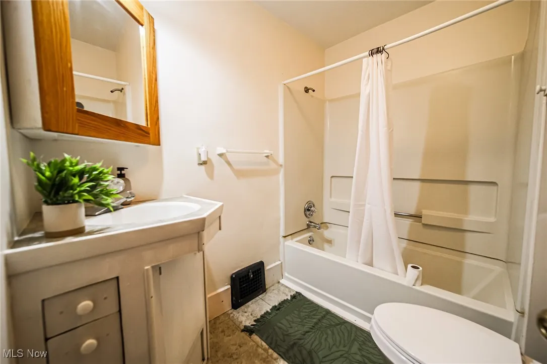 Full bath featuring shower / tub combo with curtain, vanity, toilet, and baseboards