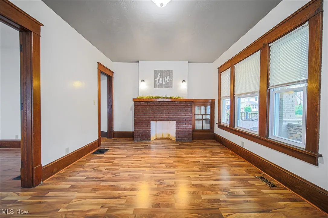 Unfurnished living room with wood finished floors, baseboards, and a brick fireplace