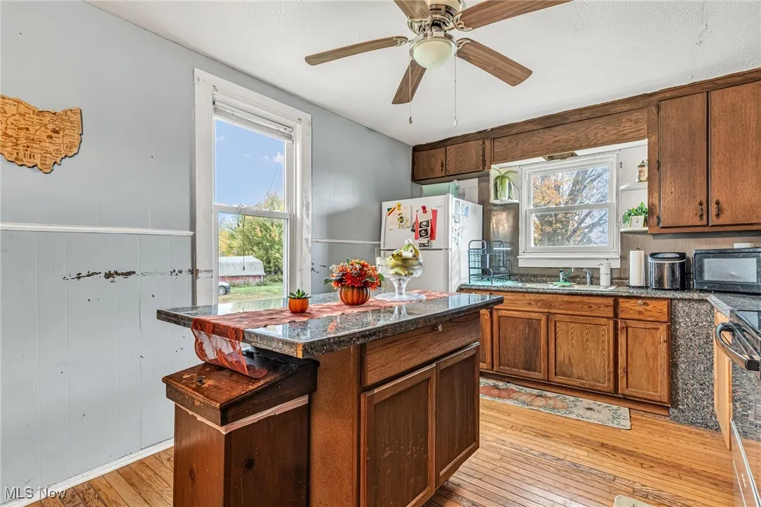 Kitchen featuring a center island, light wood finished floors, freestanding refrigerator, brown cabinetry, and stainless steel stove