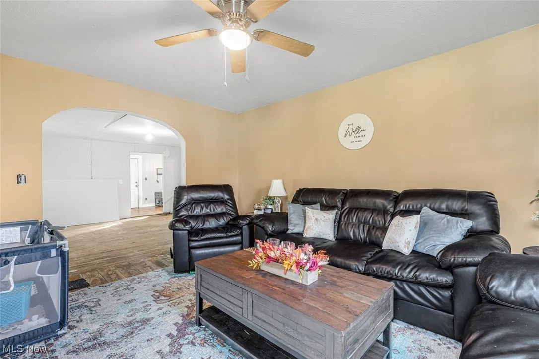 Living area with wood finished floors, arched walkways, and a ceiling fan