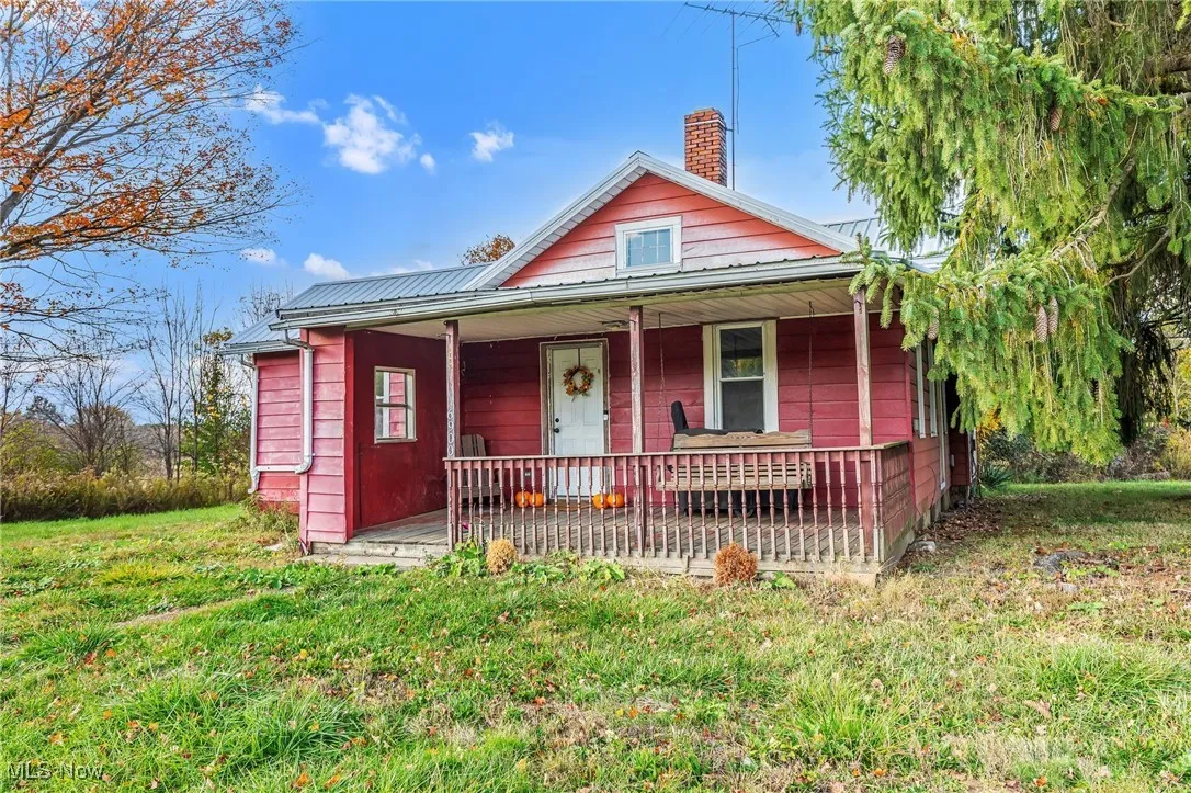 Bungalow-style home with a front lawn, a chimney, covered porch, and a metal roof