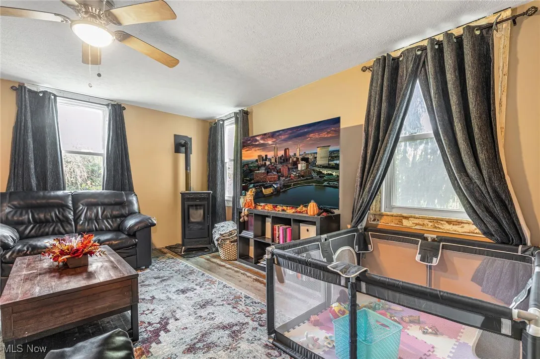 Living room featuring a wood stove, a textured ceiling, healthy amount of natural light, wood finished floors, and a ceiling fan