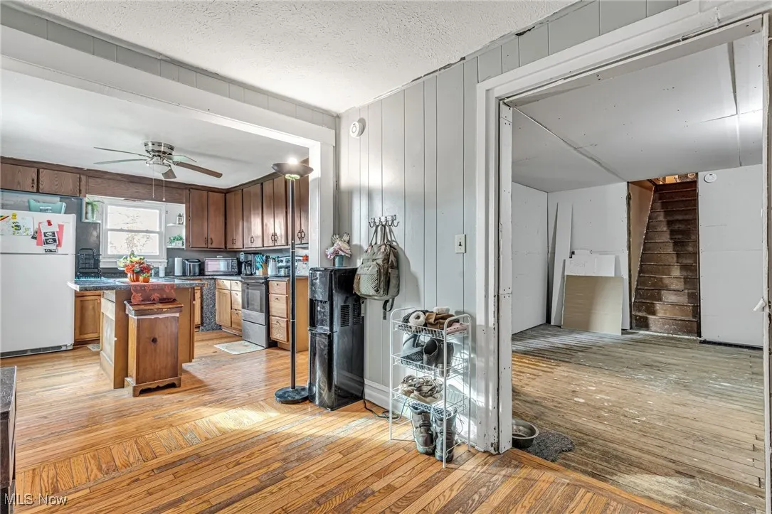 Kitchen with light wood-type flooring, freestanding refrigerator, dark countertops, wooden walls, and stainless steel electric range oven