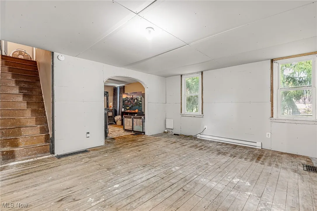 Spare room featuring arched walkways, wood-type flooring, stairs, and a baseboard heating unit